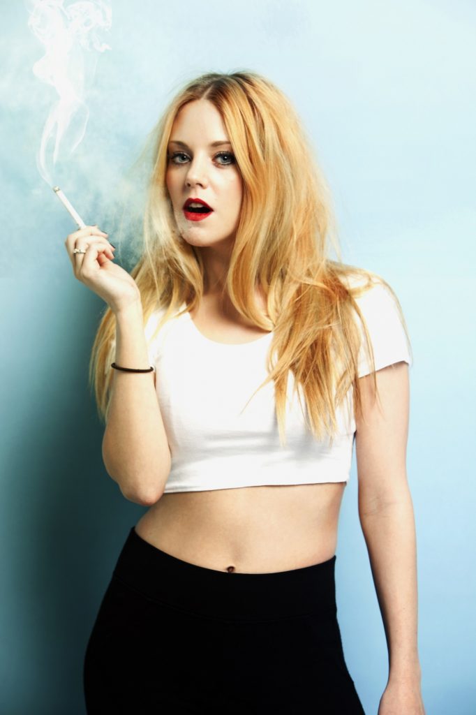 Portrait of young blond woman holding cigarette against blue background